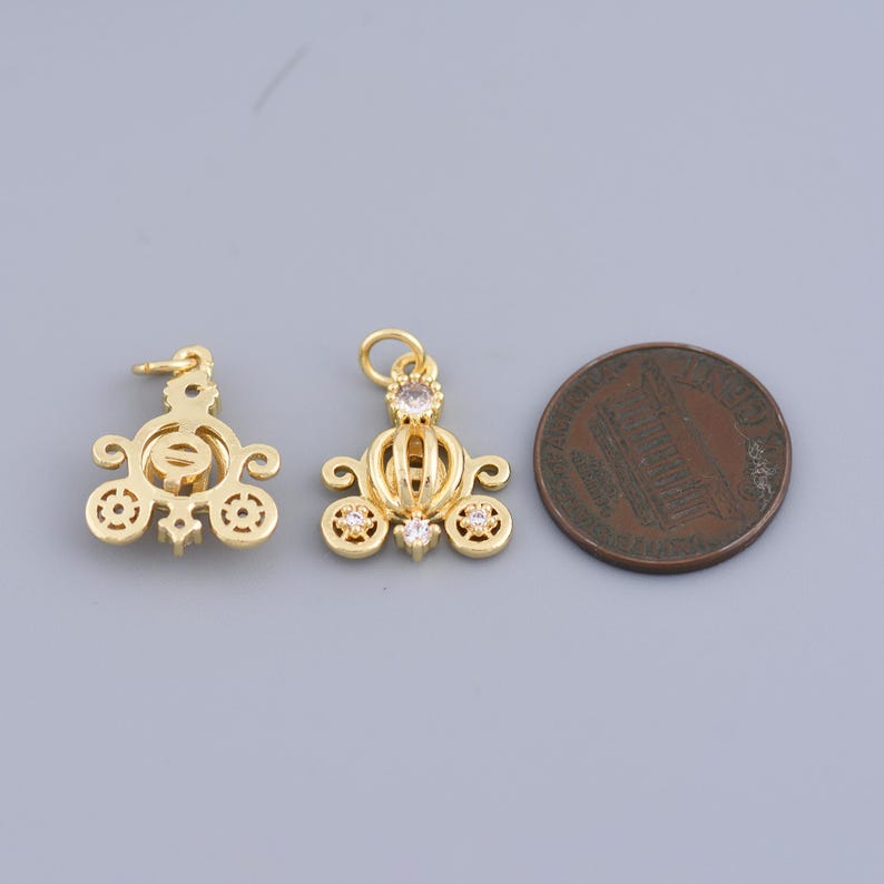 May include: Two gold-tone metal charms in the shape of a carriage with clear rhinestone accents. The charms are about the size of a US penny.