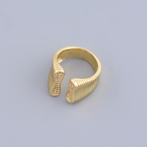 May include: A gold-toned ring with a textured band and a small gap in the front. The ring is decorated with small clear stones.