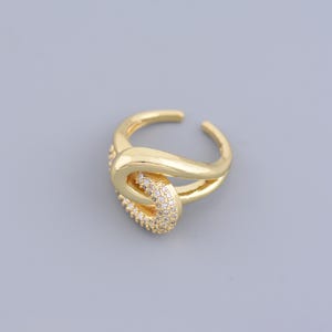 May include: A gold ring with a knot design and clear cubic zirconia stones.