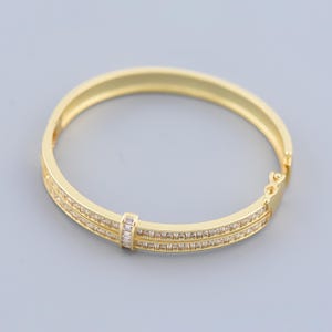 May include: A gold bangle bracelet with a double row of clear cubic zirconia stones.