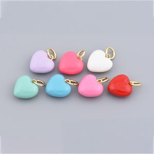 Puede incluir: Una colección de colgantes en forma de corazón en varios colores, incluyendo lavanda, rosa, blanco, verde menta, azul y rojo. Cada colgante tiene un lazo dorado para sujetar, ideal para hacer joyas o manualidades.
