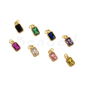 Può includere: Otto ciondoli dorati con pietre di vetro di diversi colori. Ogni ciondolo ha un anello nella parte superiore per attaccarlo a una collana o un braccialetto. Le pietre sono nere, verdi, blu, viola, rosa, bianche e gialle.
