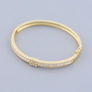 May include: A gold bangle bracelet with a row of clear cubic zirconia stones. The bracelet has a hinged clasp.