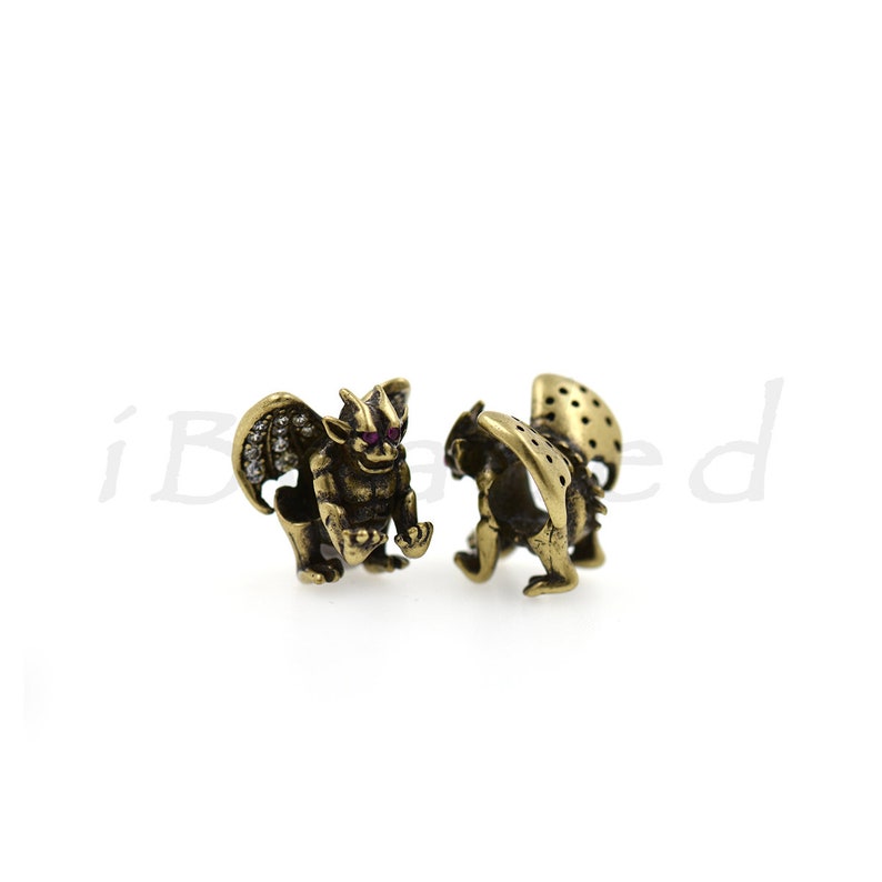 Peut inclure: Deux figurines de gargouille dor&eacute;es avec des yeux rouges. Les gargouilles se font face et ont des ailes et une surface textur&eacute;e.
