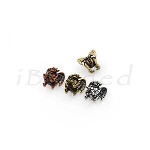 Peut inclure: Quatre petites figurines de gargouilles ail&eacute;es, chacune avec une finition diff&eacute;rente&nbsp;: cuivre, or, argent et bronze. Chaque gargouille a un petit bijou rose sur la poitrine.
