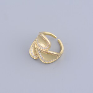 May include: A gold ring with a unique design featuring three overlapping, teardrop-shaped pieces, each adorned with a row of sparkling clear stones.