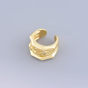 Puede incluir: Pendiente de aro dorado con diseño geométrico y pequeñas piedras transparentes.