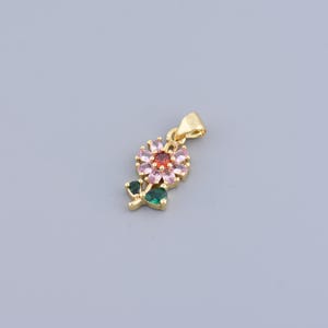 May include: A gold-tone pendant featuring a pink and red flower with green leaves. The flower has a red centre and is surrounded by pink stones.