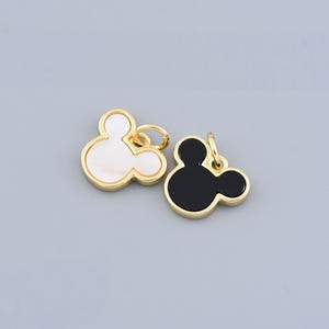 May include: Two gold-colored charms in the shape of Mickey Mouse's head. One charm is black and the other is white with a pearlescent finish.