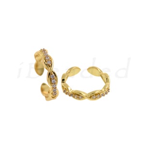 May include: A pair of gold ear cuffs with a twisted design and clear cubic zirconia stones.