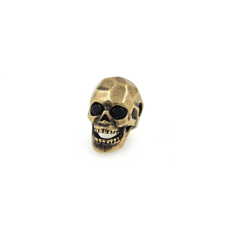 May include: A gold-colored skull charm with black eyes. The skull is detailed with a toothy grin.