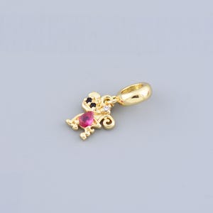 May include: Gold-toned charm featuring a stylized mouse design. The mouse has black eyes, a pink heart-shaped gem, and a small white gem. The charm has a loop for attaching to a bracelet or necklace.