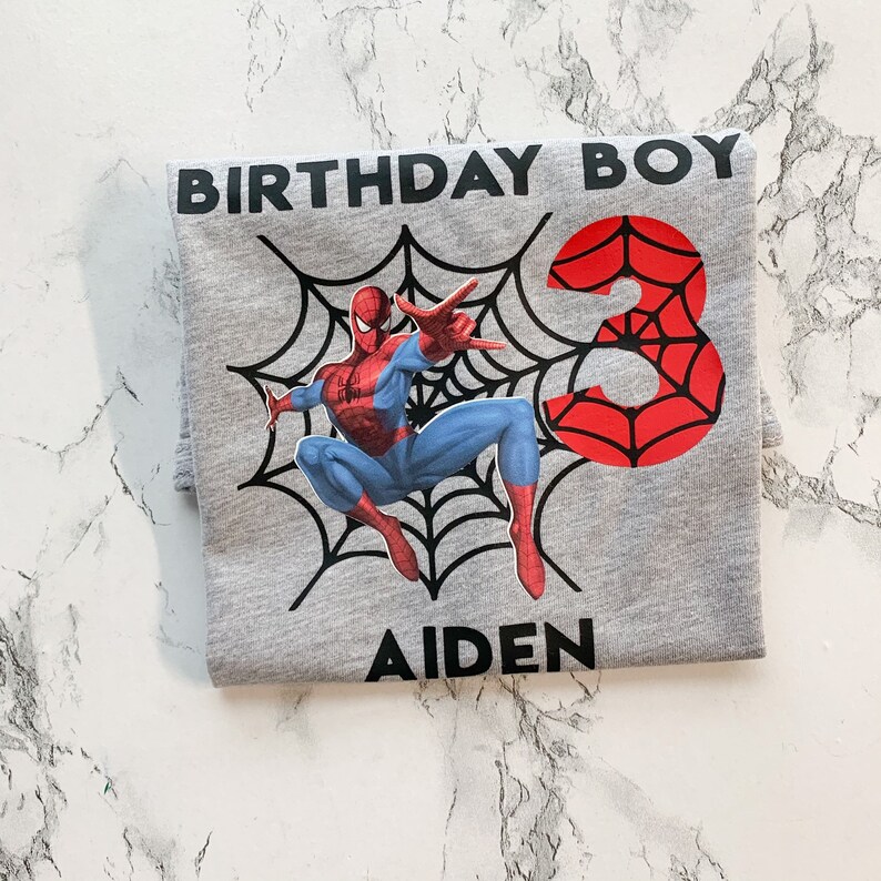 May include: Gray t-shirt with a Spiderman graphic, a red web design with the number 3, and the text "Birthday Boy" and "Aiden".