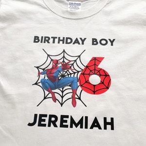 May include: White t-shirt with a red and blue Spiderman graphic, a black web, and the text "Birthday Boy" and "Jeremiah" in black.