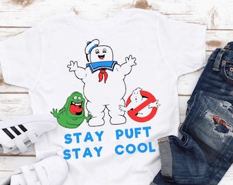 Könnte beinhalten: Weißes T-Shirt mit einem Cartoon-Bild von Stay Puft Marshmallow Man aus Ghostbusters. Das Shirt zeigt außerdem einen grünen Geist und ein rotes Schild mit der Aufschrift "Kein Geist". Der Text "Stay Puft Stay Cool" ist auf das Shirt gedruckt.