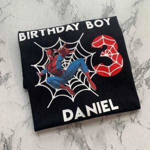 May include: Black t-shirt with a white spider web design, a red and black spider-man character, and the number 3 in red with a spider web design. The text "Birthday Boy" and "Daniel" are in white.