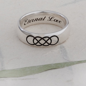 Op de afbeelding: Een zilveren ring met een gegraveerd oneindigheidssymbool en de woorden "Eternal Love".