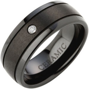 May include: Black ceramic ring with a single diamond set in the center and two black lines around the band. The ring is engraved with the word "CERAMIC".