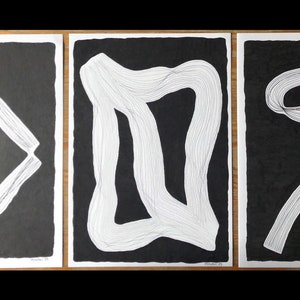 May include: Three black and white abstract art prints with white line drawings on a black background. The first print features a white line drawing of a triangle shape. The second print features a white line drawing of a rectangle shape. The third print features a white line drawing of a squiggly line.