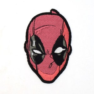May include: Embroidered patch featuring a red and black Deadpool face with a white background.