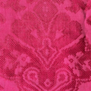 May include: Close-up of a vibrant pink fabric with a detailed, geometric pattern. The design features repeating shapes and textures in varying shades of pink, creating a rich, textured appearance. The fabric's surface appears soft and slightly textured.