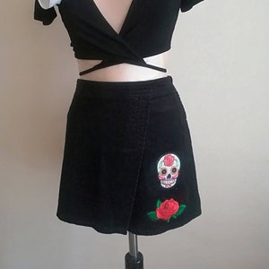 May include: Black wrap crop top with a black corduroy mini skirt. The skirt has a sugar skull and rose embroidery.
