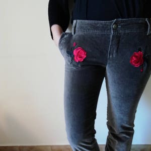 Può includere: Pantaloni di velluto grigio con rose rosse ricamate sulle tasche anteriori.