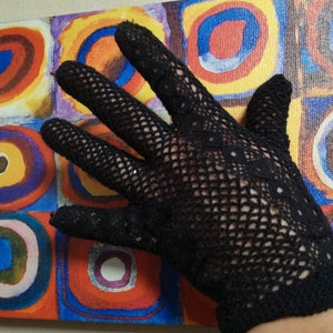 May include: A black crocheted lace glove with a fine mesh pattern. The glove is laid flat on a colorful abstract painting.