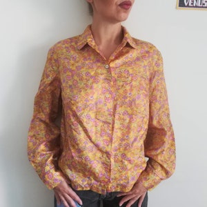 May include: A yellow long-sleeved shirt with a pink and purple floral pattern. The shirt has a button-up front and a collared neckline.