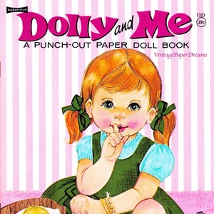 May include: A vintage "Dolly and Me" paper doll book cover. The image shows a young girl with red pigtails, wearing a green dress, with a finger to her lips. A baby doll sleeps in a wooden bed, and a red ball is on the floor.
