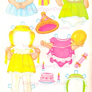 Op de afbeelding: Een vintage papieren poppenset met diverse outfits en accessoires. De set bevat een gele jurk, een blauwe jurk, een roze feesthoed, een verjaardagstaart en een cadeauverpakking. De tekst "Vintage Paper Dreams" is zichtbaar.