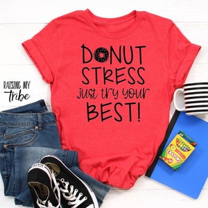 May include: Red t-shirt with the text "Donut stress just try your best!" in black lettering. A donut with pink frosting and sprinkles is above the word "Donut".