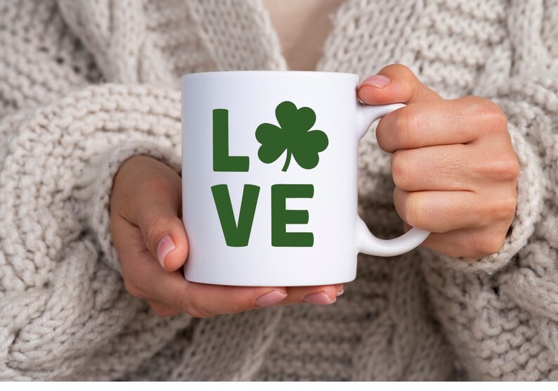 Op de afbeelding: Een witte keramische mok met een groene klaver en het woord "LOVE" in groene letters.