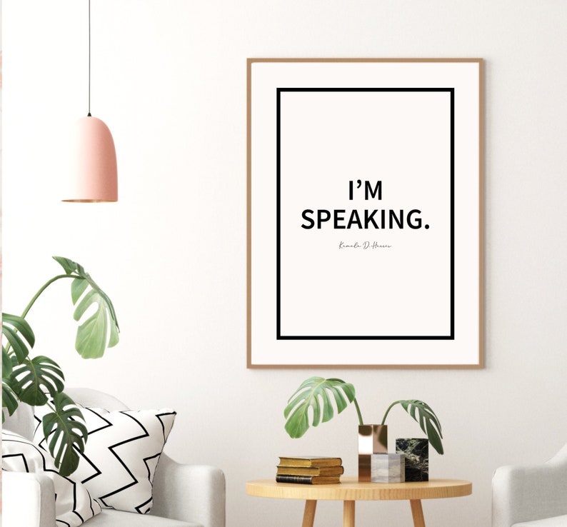 May include: A black and white framed print with the text "I'M SPEAKING." and the name "Emily D. Herrera" in a smaller font below. The print is hanging on a white wall.