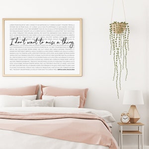 May include: A framed print with a black and white design. The print features a quote that reads "I don't want to miss a thing". The print is hanging on a white wall above a pink bed.