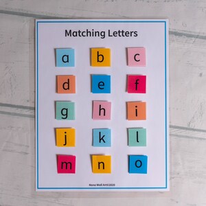 Op de afbeelding: Een kleurrijk educatief matchingspel voor kinderen met de letters van het alfabet, gedrukt op individuele vierkanten papier. De letters zijn gerangschikt in rijen, met elke letter in een andere kleur.