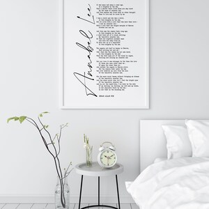 May include: A white framed print of a poem titled "Annabel Lee" by Edgar Allan Poe. The poem is printed in black ink on a white background. The print is hanging on a white wall above a white nightstand with a white alarm clock.