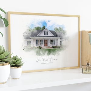 Puede incluir: Una impresi&oacute;n en acuarela enmarcada de una casa blanca con techo negro y puerta marr&oacute;n. La impresi&oacute;n est&aacute; en un marco dorado y tiene el texto "Our First Home" y "Santa Monica, CA EST 2020". La impresi&oacute;n se exhibe en un estante blanco con plantas.