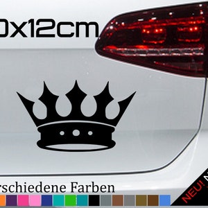 Puede incluir: Pegatina negra en forma de corona con tres puntas en la parte superior y una banda con tres puntos. La pegatina mide 20 por 12 centímetros y se muestra en la parte trasera de un coche blanco. El texto "21 verschiedene Farben" está debajo de la pegatina, y una fila de 21 muestras de colores está debajo del texto.