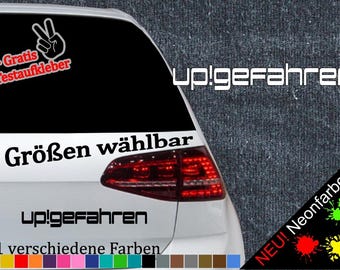 May include: A white car with a black and white sticker that says "up!gefahren" and "6 Größen wählbar". The sticker also includes a peace sign and the text "+ Gratis Testaufkleber". The car has a red taillight and a black and white sticker that says "NEU! Neonfarben" with colorful paint splatters.