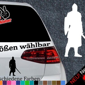 Puede incluir: Una silueta en blanco y negro de un caballero sosteniendo una espada, con el texto "6 Größen wählbar" y "21 verschiedene Farben" debajo. La imagen está en un coche con una luz trasera roja.