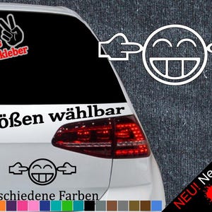 Könnte beinhalten: Ein weißes Auto mit einem schwarz-weißen Aufkleber eines Smiley-Gesichts mit den Händen über den Ohren. Der Aufkleber sagt "6 Größen wählbar" und "21 verschiedene Farben". Außerdem ist ein Aufkleber mit einem Peace-Zeichen mit dem Text "+ Gratis Testaufkleber" zu sehen.