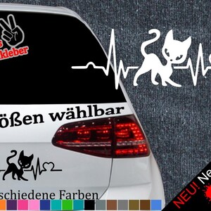 May include: A white cat silhouette with a heartbeat graphic and a heart. The text "6 Größen wählbar" and "21 verschiedene Farben" are below the graphic. The image is on a car's rear window.