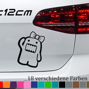 May include: A black and white sticker of a cartoon character with a bow on its head. The sticker is 15 x 12 cm and is shown on the back of a white car. The text "18 verschiedene Farben" is visible below the sticker.