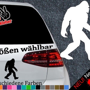 May include: A white silhouette of Bigfoot walking, with the text "6 Größen wählbar" and "21 verschiedene Farben" below. The image is on a white car with a red taillight. The text "+ Gratis Testaufkleber" is in the top left corner. The text "NEU! Neonfarben" is in the bottom right corner with three paint splatters in red, yellow, and green.