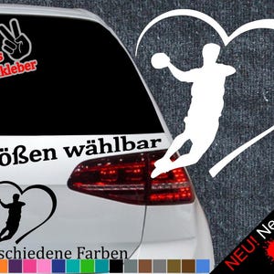 Könnte beinhalten: Ein weißes Auto mit einem schwarzen herzförmigen Aufkleber, der eine Silhouette einer Person beim Handballspielen zeigt. Der Aufkleber enthält auch den Text "6 Größen wählbar" und "21 verschiedene Farben".