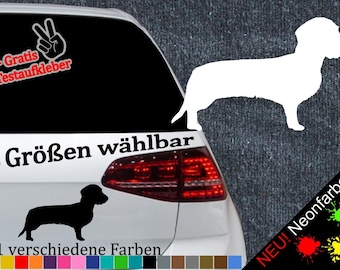 May include: A white car with a black dachshund silhouette sticker on the back window. The sticker says "6 Größen wählbar" and "21 verschiedene Farben". There is also a sticker of a peace sign with the text "+ Gratis Testaufkleber".