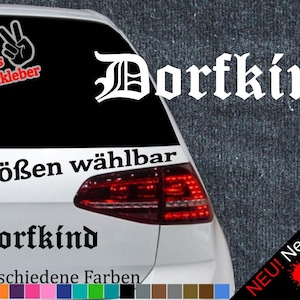 Könnte beinhalten: Ein weißes Auto mit einem schwarz-weißen Aufkleber, auf dem "Dorfkind" in gotischer Schrift steht. Der Aufkleber befindet sich auf der Heckscheibe des Autos. Das Auto hat auch einen Aufkleber, auf dem "6 Größen wählbar" und "21 verschiedene Farben" steht.