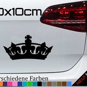 Puede incluir: Adhesivo negro con forma de corona, de aproximadamente 20 x 10 cm, colocado en un coche blanco. El texto "20x10cm" está encima de la corona. Debajo de la corona, el texto "21 verschiedene Farben" y una paleta de colores son visibles.