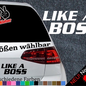 Może przedstawiać: Biały samochód z czarnym tylnym oknem. Tylne okno ma naklejkę z napisem "LIKE A BOSS" białymi literami. Naklejka jest otoczona czerwoną ramką. Samochód ma również naklejkę z napisem "6 Größen wählbar" czarnymi literami. Samochód ma czerwone tylne światło. Samochód jest zaparkowany na parkingu. Jest znak z napisem "NEU! Neonfarben" czarnymi literami z czerwoną, zieloną i żółtą plamą farby.